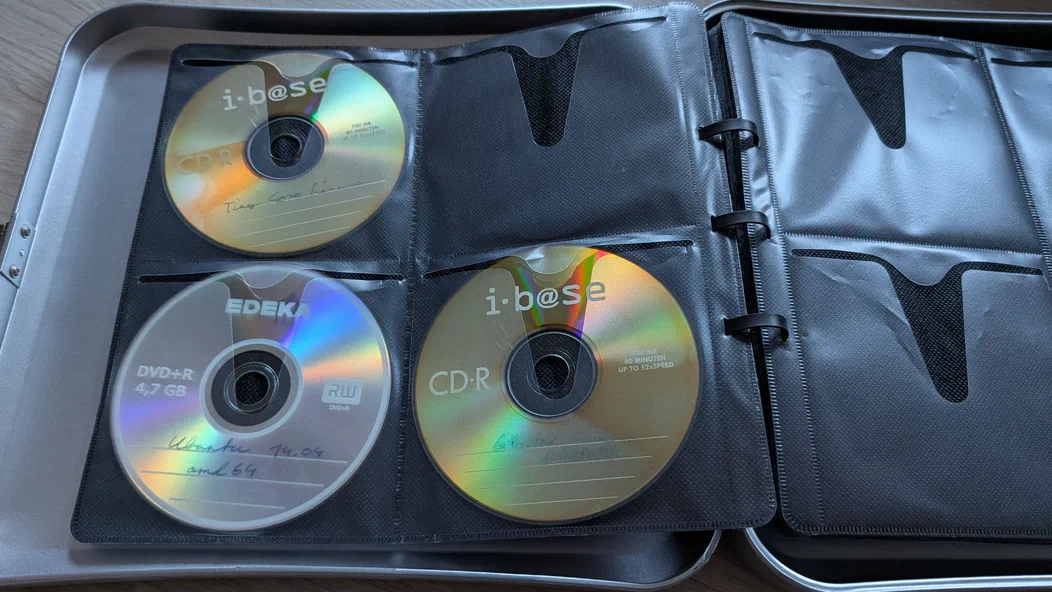 An open metal case with disc sleeves holding three labeled discs: a “Tiny Core Linux” CD, an “Ubuntu 14.04 amd64” DVD, and a “GParted Live” CD. The remaining sleeves are empty.